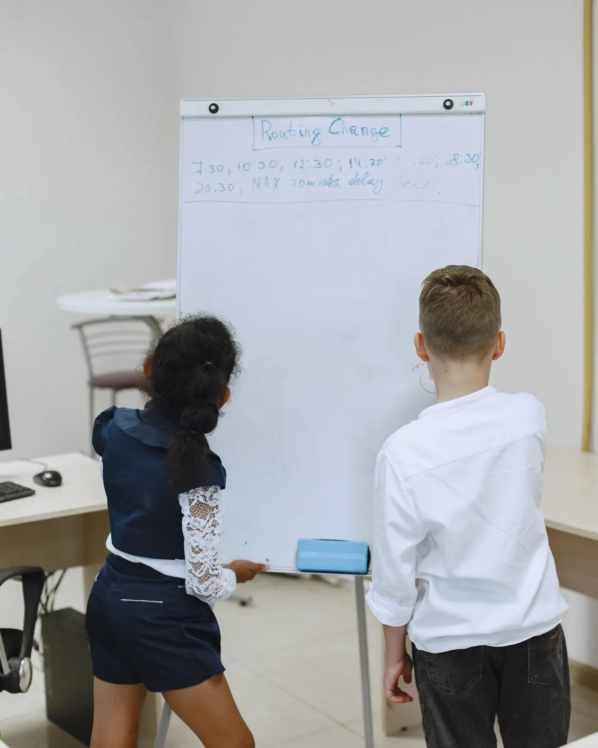 Two children presenting together at a whiteboard, seen from behind