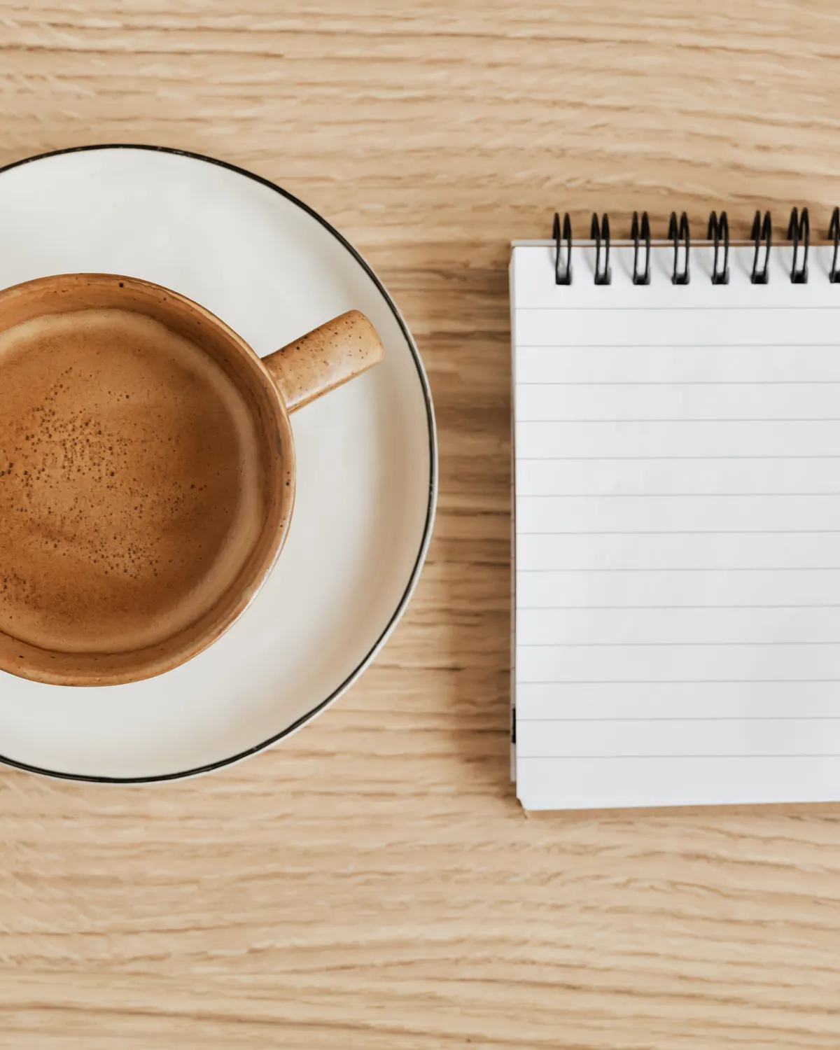A coffee cup, blank notebook and pen arranged on a wooden table