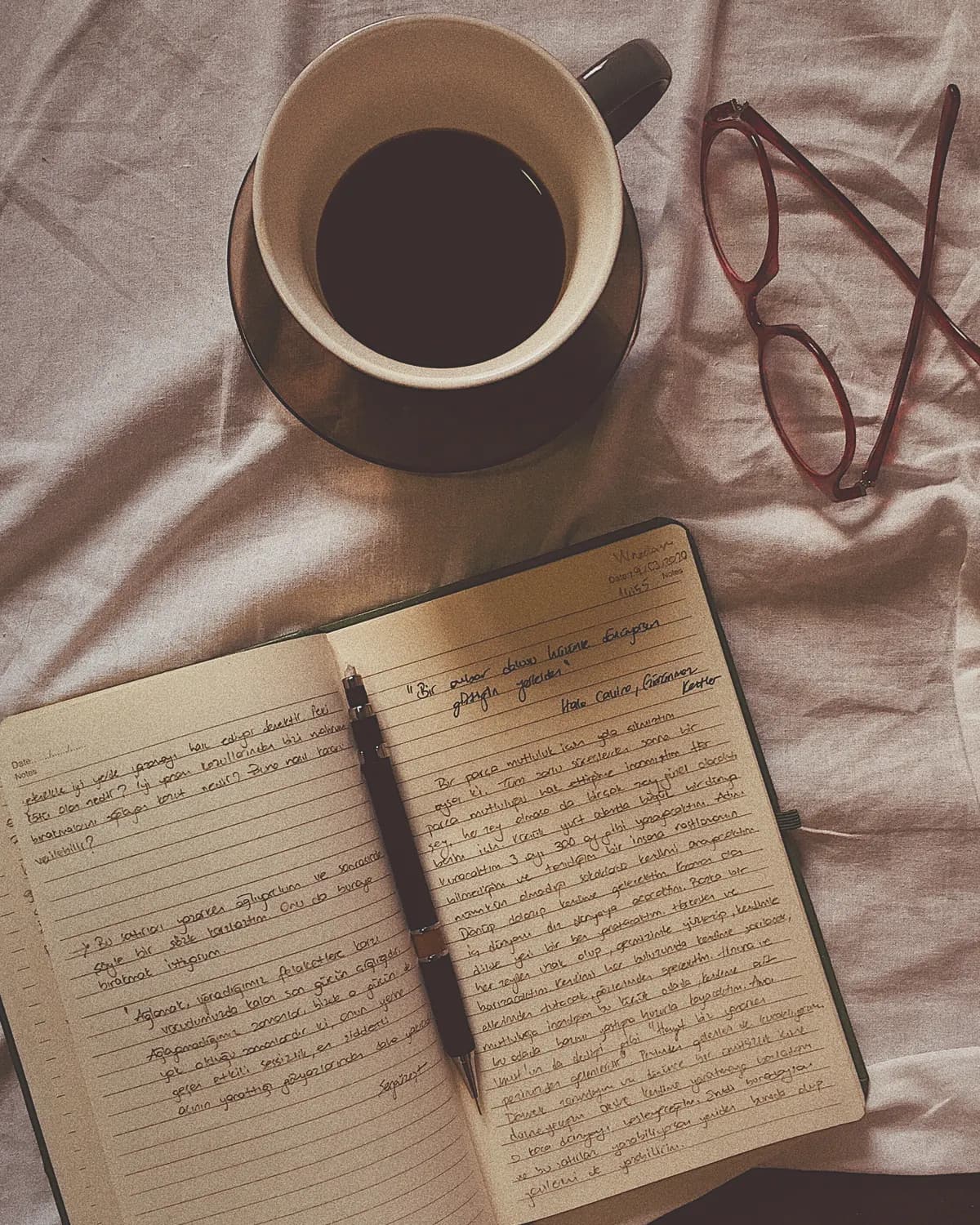 A notebook, coffee and glasses on a linen surface