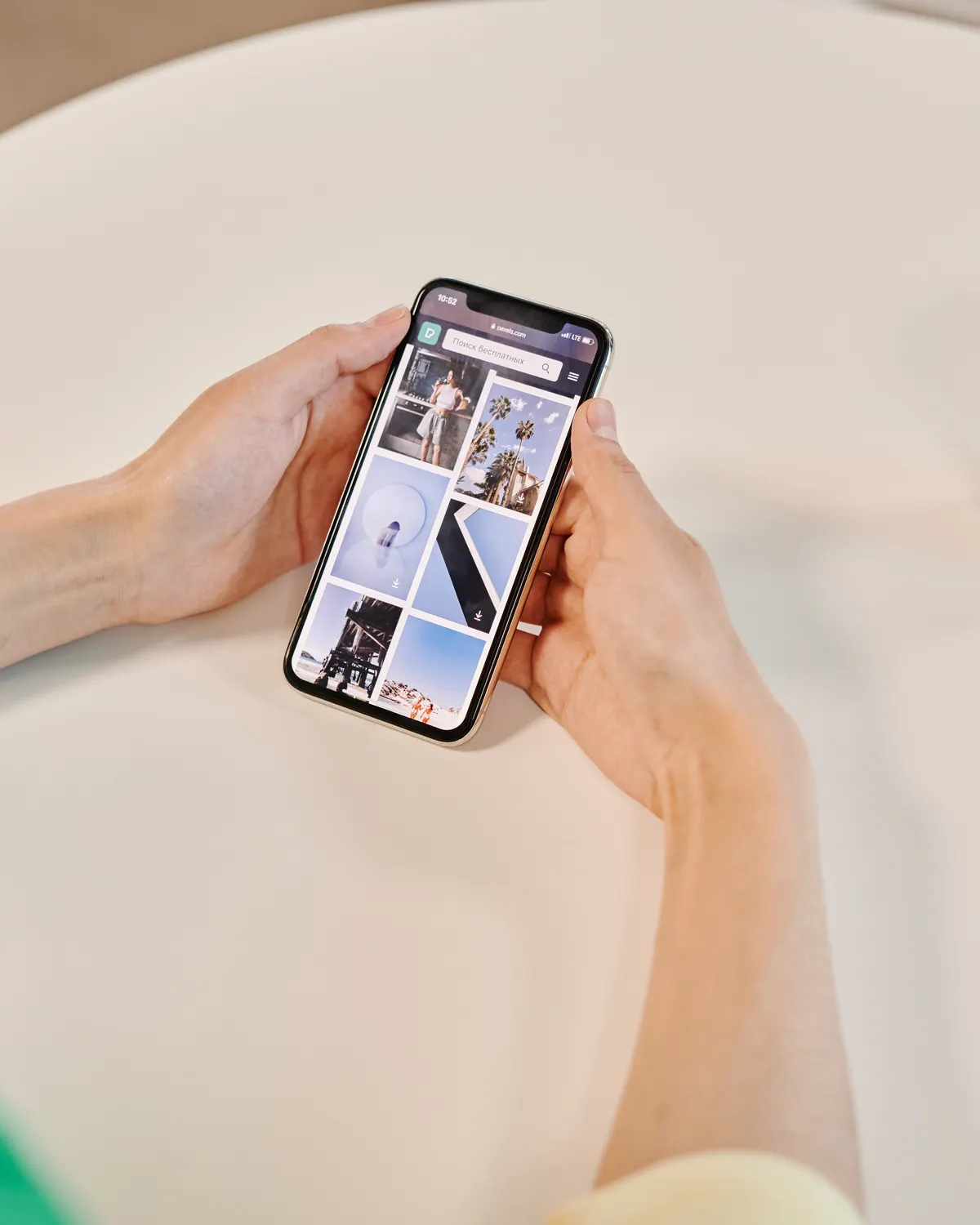 Hands holding a phone beside a coffee cup at a bright table